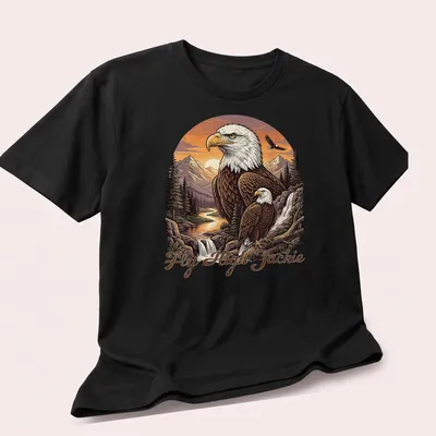Illustration of a Bald Eagle flying over a mountain scene with the text Fly High Jackie — printed on a unisex t-shirt (angled view)