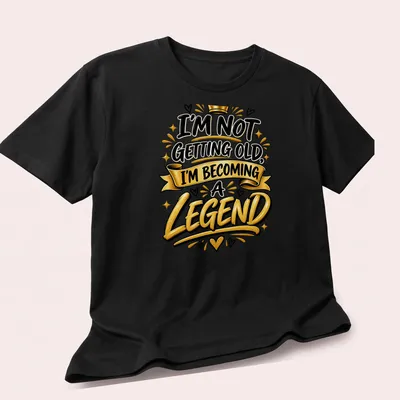 Bold typography t-shirt with the text I'm Not Getting Old, I'm Becoming a Legend in black, gold, and white. — printed on a unisex t-shirt (angled view)