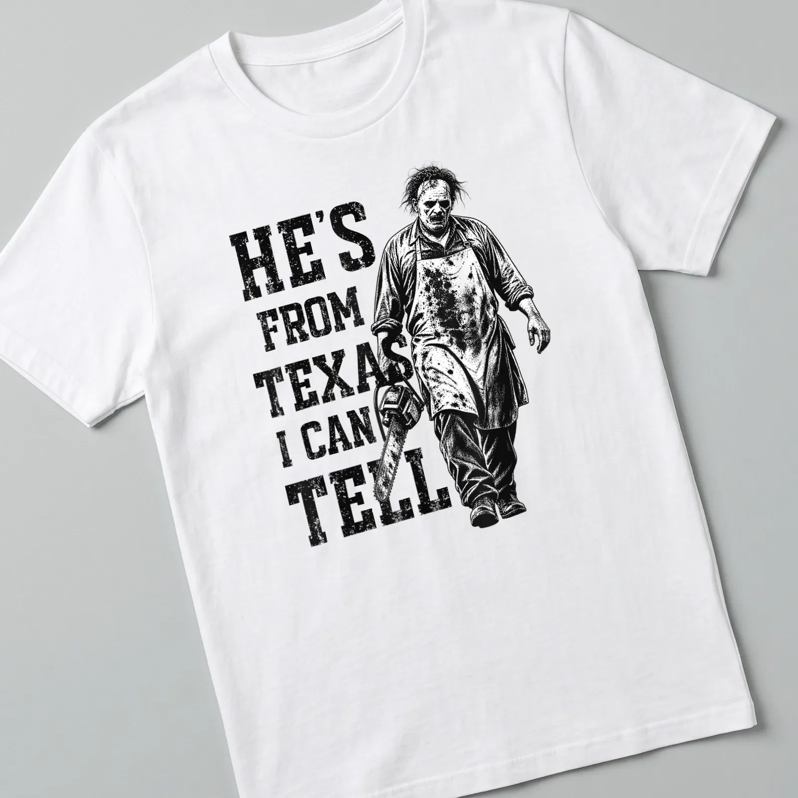 Vintage horror tee featuring a chainsaw character with the text 'He's from Texas I can tell' — printed on a unisex t-shirt