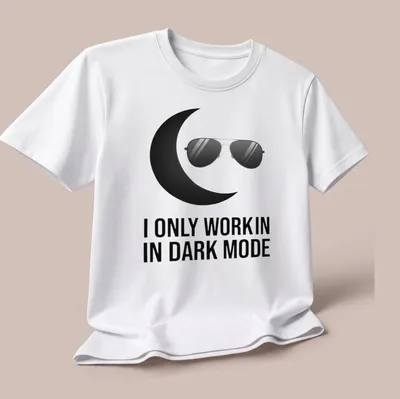 Minimalist design with black sunglasses and crescent moon above the text 'I ONLY WORK IN DARK MODE' — printed on a unisex t-shirt (angled view)