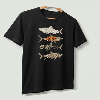 Illustrative t-shirt featuring a shark skeleton, pumpkin, and mummy elements for Halloween — printed on a unisex t-shirt (angled view)
