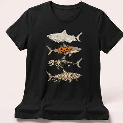 Illustrative t-shirt featuring a shark skeleton, pumpkin, and mummy elements for Halloween — printed on a women's shirt
