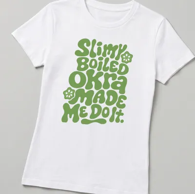 Playful typography t-shirt featuring okra-themed humor in green bubble letters — printed on a women's shirt