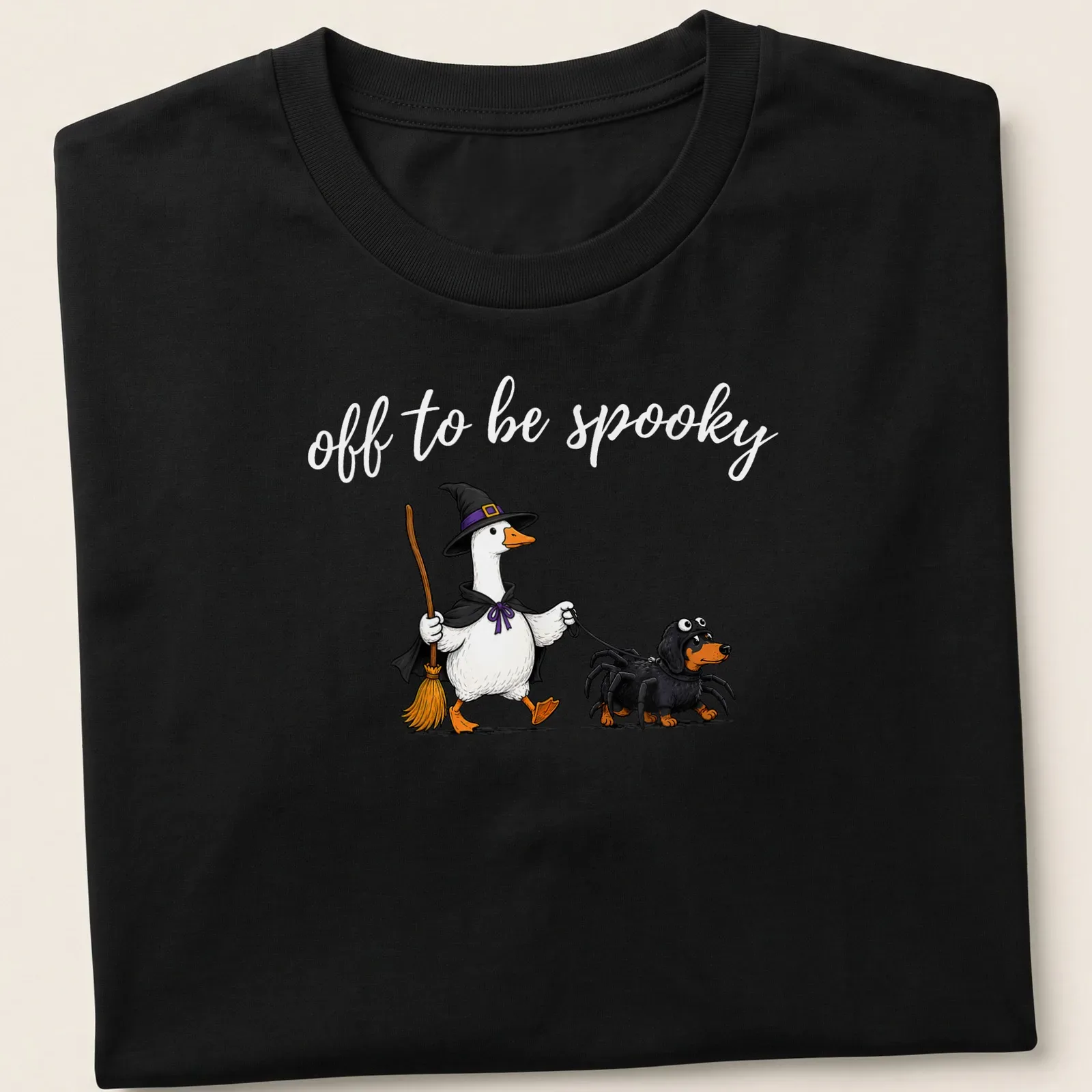 Cartoon of a witch goose walking a spider dachshund with spooky text — printed on a unisex t-shirt