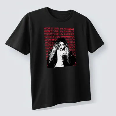 Bold graphic tee featuring the text 'WOR$T GIRL IN AMERICA' with an illustration of a woman with curly hair. — printed on a unisex t-shirt (angled view)