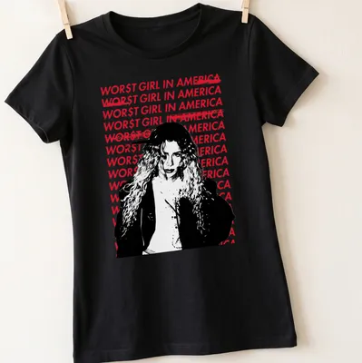 Bold graphic tee featuring the text 'WOR$T GIRL IN AMERICA' with an illustration of a woman with curly hair. — printed on a women's shirt